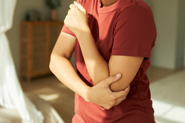 Cropped closeup indoor shot of black unrecognizable person touching and massaging hurt elbow,...
