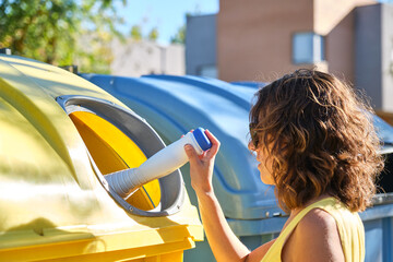 young woman throwing a container into the yellow recycling bin