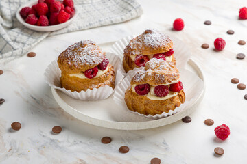 profiteroles with cream and fresh raspberries on white plate on white marble table
