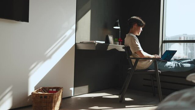 Sunny young Asian brunet man working on laptop at home