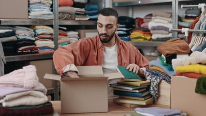 Disabled male volunteer folding books and putting it into the cupboard box at the warehouse. Humanitarian aid and donating concept. Second hand
