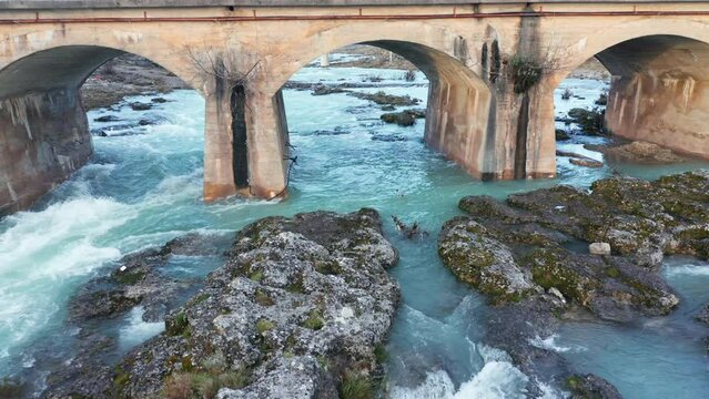 Blue river flowing under an arch bridge through beautiful rocky landscape. Aerial drone view of Cijevna (Cem, Cemi) stream in Montenegro, Europe.