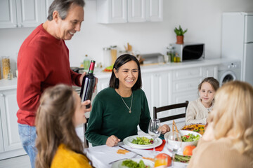 Multiethnic woman sitting near family and tasty thanksgiving dinner in kitchen