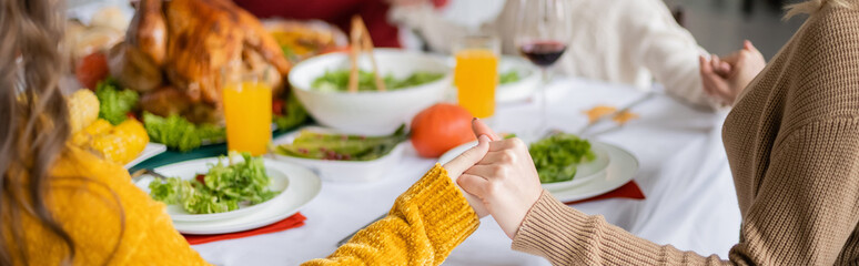 Cropped view of family holding hands near thanksgiving dinner with turkey at home, banner