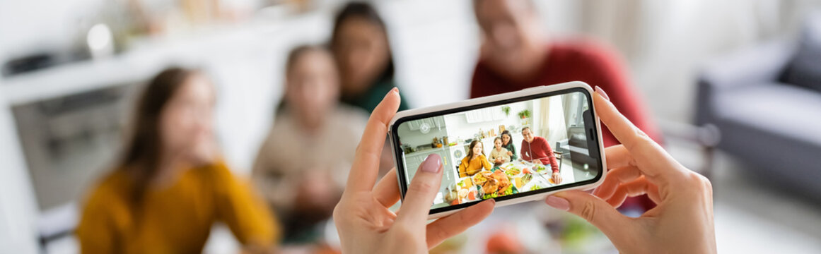 Woman taking photo of multicultural family and thanksgiving dinner at home, banner