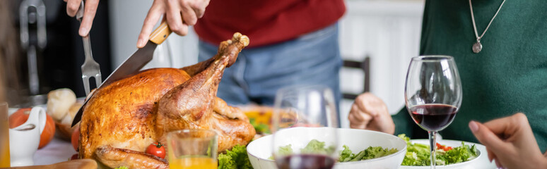 Cropped view of senior man cutting delicious thanksgiving turkey near dinner at home, banner