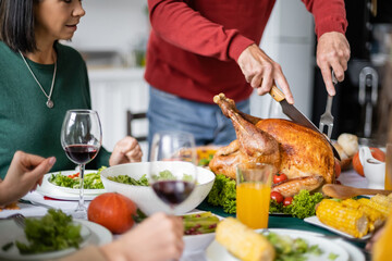 Cropped view of senior man cutting delicious thanksgiving turkey near women and wine at home