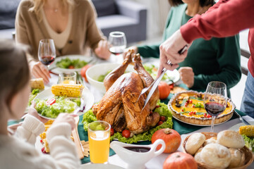 Grandparent cutting turkey near blurred family and kid celebrating thanksgiving at home