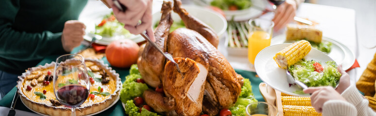 Partial view of girl holding plate near grandparent cutting thanksgiving turkey at home, banner
