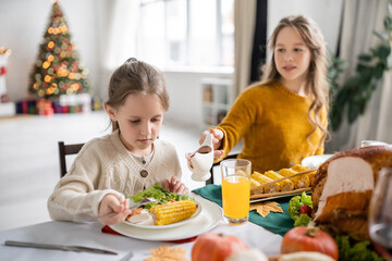 Girl looking at salad and corn near blurred sister with sauce during thanksgiving dinner at home