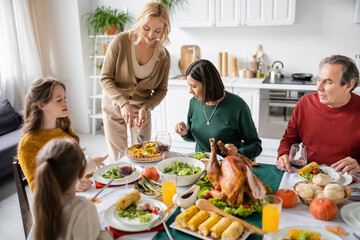 Smiling woman cutting pie near multiethnic parents and kids during thanksgiving dinner at home