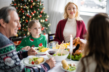 cheerful woman looking at family during festive dinner near christmas tree