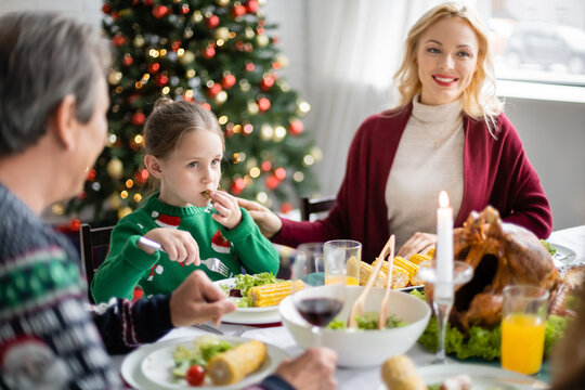 girl with fork having christmas dinner near blurred grandfather and smiling mom