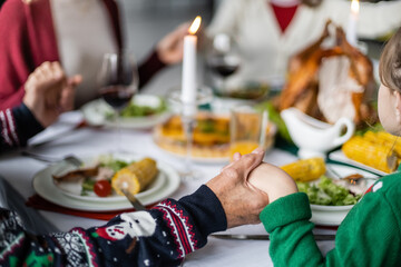 partial view of family holding hands during pray before thanksgiving dinner on blurred background