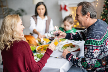 cheerful relatives clinking glasses of red wine near delicious christmas dinner and blurred family