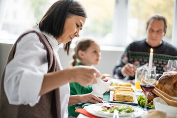 multiracial woman holding sauce boat during festive thanksgiving dinner with family