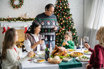 mature man toasting with wine glass near interracial family during festive christmas dinner