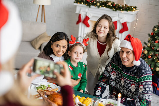 blurred woman taking photo of daughters with interracial grandparents near festive dinner