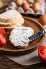 bread with butter, cream cheese, eggs next to tomatoes and a knife. breakfast on a wooden table