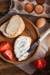 bread with butter, cream cheese, eggs next to tomatoes and a knife. breakfast on a wooden table
