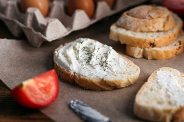 bread with butter, cream cheese, eggs next to tomatoes and a knife. breakfast on a wooden table