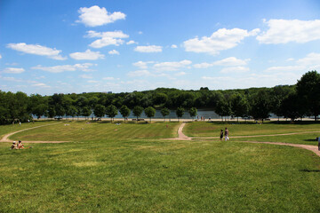 A path in a huge meadow with a green lawn and sunbathing people in the meadow