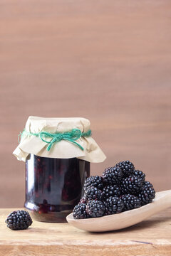 Jar of homemade natural blackberry jam in an eco-friendly package with fresh ripe large berries on a wooden table on a brown background