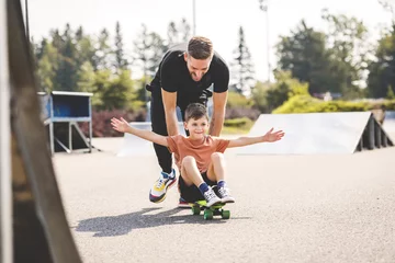 Rollo young boy learning to ride skateboard as father teaches him in the suburb street having fun. © Louis-Photo