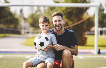 man with child playing football outside on field