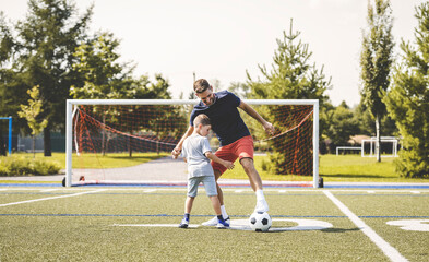 man with child playing football outside on field