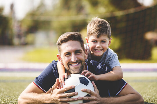 Man With Child Playing Football Outside On Field