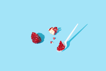 Red pomegranate slices and seeds on spoon isolated on blue background. Autumn fruit concept. Minimal style.