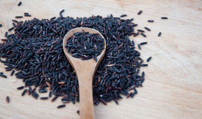 Heap of black rice in a spoon on a wooden table.