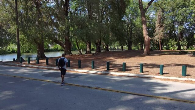 aerial footage of an African American man walking through a gorgeous summer landscape at Lake Evans at Fairmount Park surrounded by rippling water and lush green trees, grass and plants in Riverside