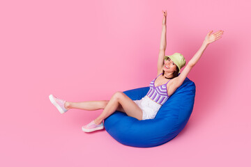 Photo of cheerful lady have fun hands up carefree emotions sit blue white bean chair isolated...