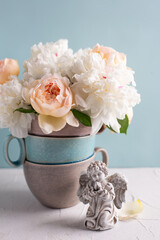Postcard with angel and romantic summer roses and peonies flowers  against blue  wall in vase. Selective focus. Still life.  Place for text. Romantc concept..