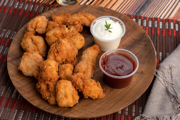 Chicken nuggets on a round wooden plate with two bowls of red sauce and white cheese sauce and glass of beer