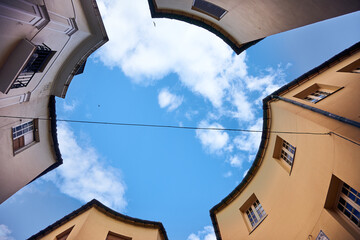 Blue sky with clouds seen from the ground with buildings forming a circle.