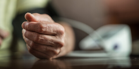 Fototapeta premium Older man measures his blood pressure with digital medical instrument. Hand of person lies on table during medical examination.