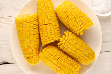 Several fragrant boiled corn with a white plate on a wooden table, macro, top view.