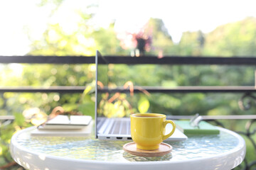 Laptop side view and yellow coffee cup with notebooks on white glass table outdoor relaxing balcony
