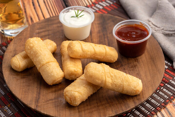 typical Venezuelan fried cheese tequeños on a round wooden plate with two sauces and hand dipping...