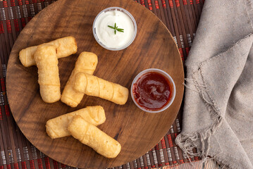 typical Venezuelan fried cheese tequeños on a round wooden plate with two sauces and hand dipping the tequeño in red sauce