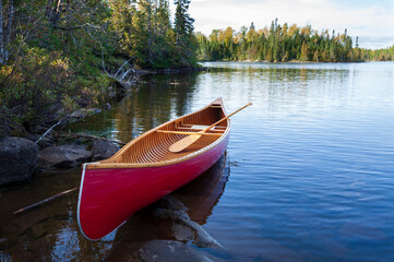 Red wood canoe on the shore of a Boundary Waters lake in morning light during autumn - Powered by Adobe