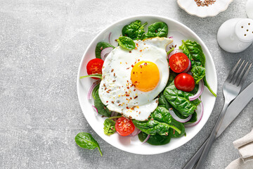 Fried egg with fresh spinach tomato salad for healthy breakfast, top view