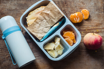 schoolboy lunch box with thermos on wooden background.apple,tangerine,sandwich in lunchbox and...
