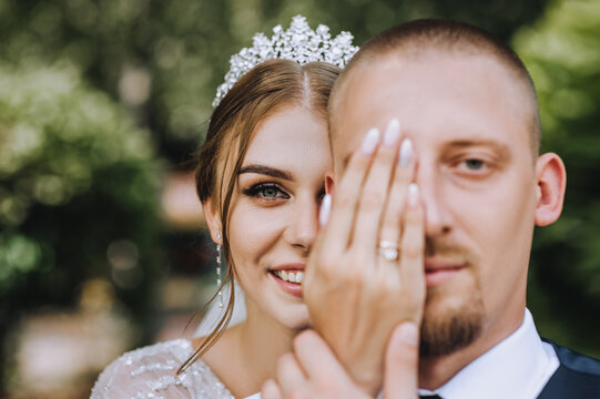 A beautiful, smiling bride with a diadem covers half of the face of the bearded groom with her hand. wedding photography.