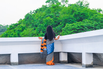 Young woman standing alone on a rooftop looking at the beautiful green mountains nature view. Tranquility, freedom, nature, vacation, and adventure concept.