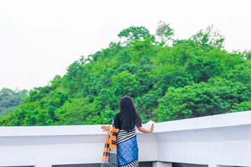 Young woman standing alone on a rooftop looking at the beautiful green mountains nature view. Tranquility, freedom, nature, vacation, and adventure concept. - Powered by Adobe