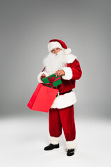 Santa claus putting present with bow in shopping bag on grey background.